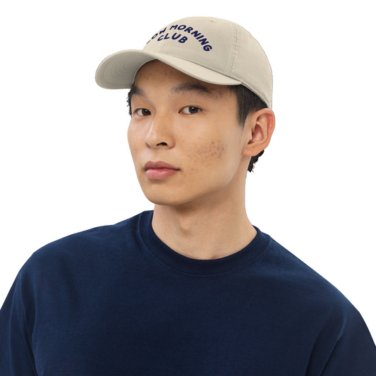 Person wearing a beige cap with text and a navy blue shirt on a white background